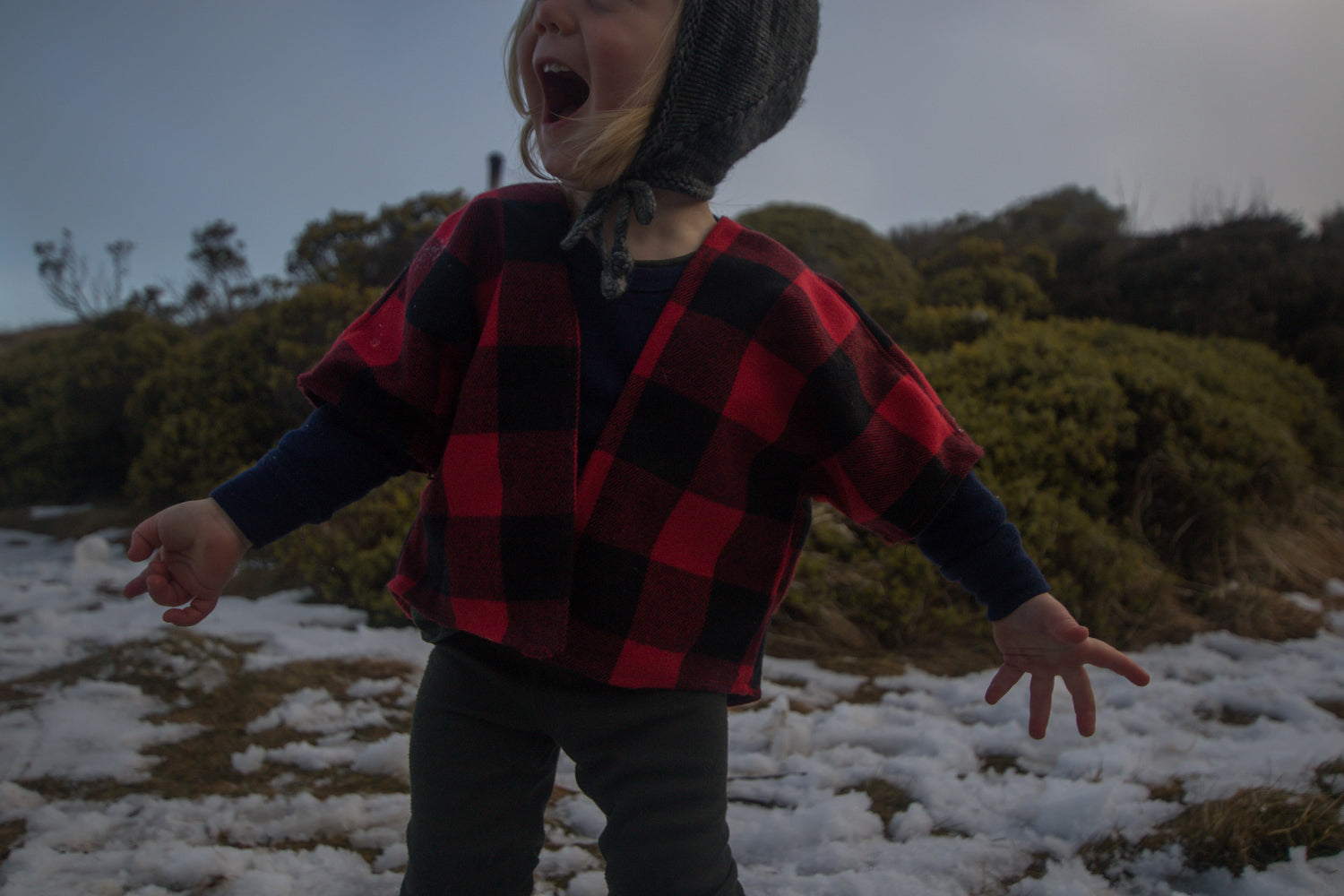 Child wearing a red and black checkered shirt in a snowy landscape