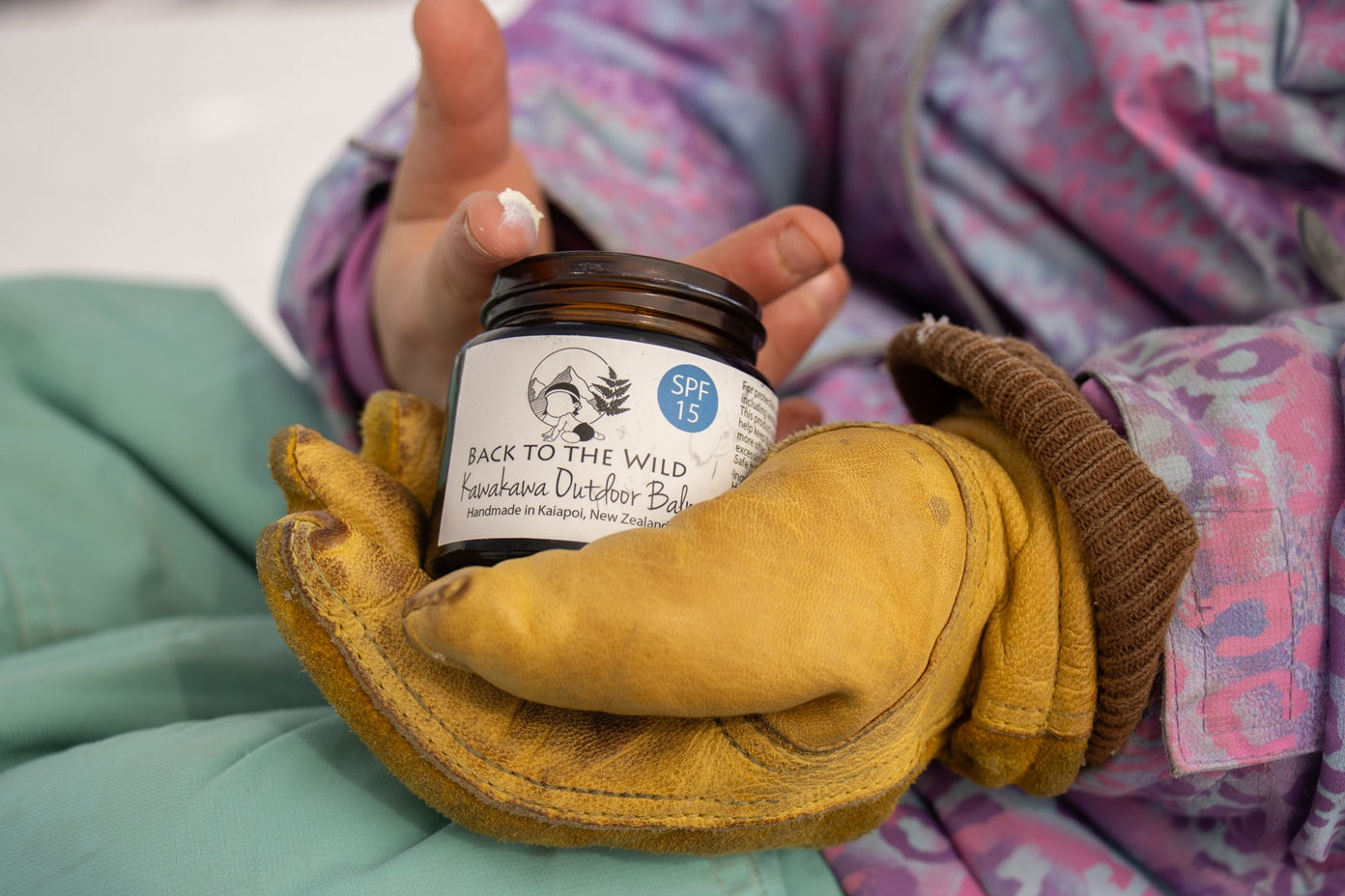 Hand holding a jar of 'Back to the Wild' sunscreen with gloves on a soft surface