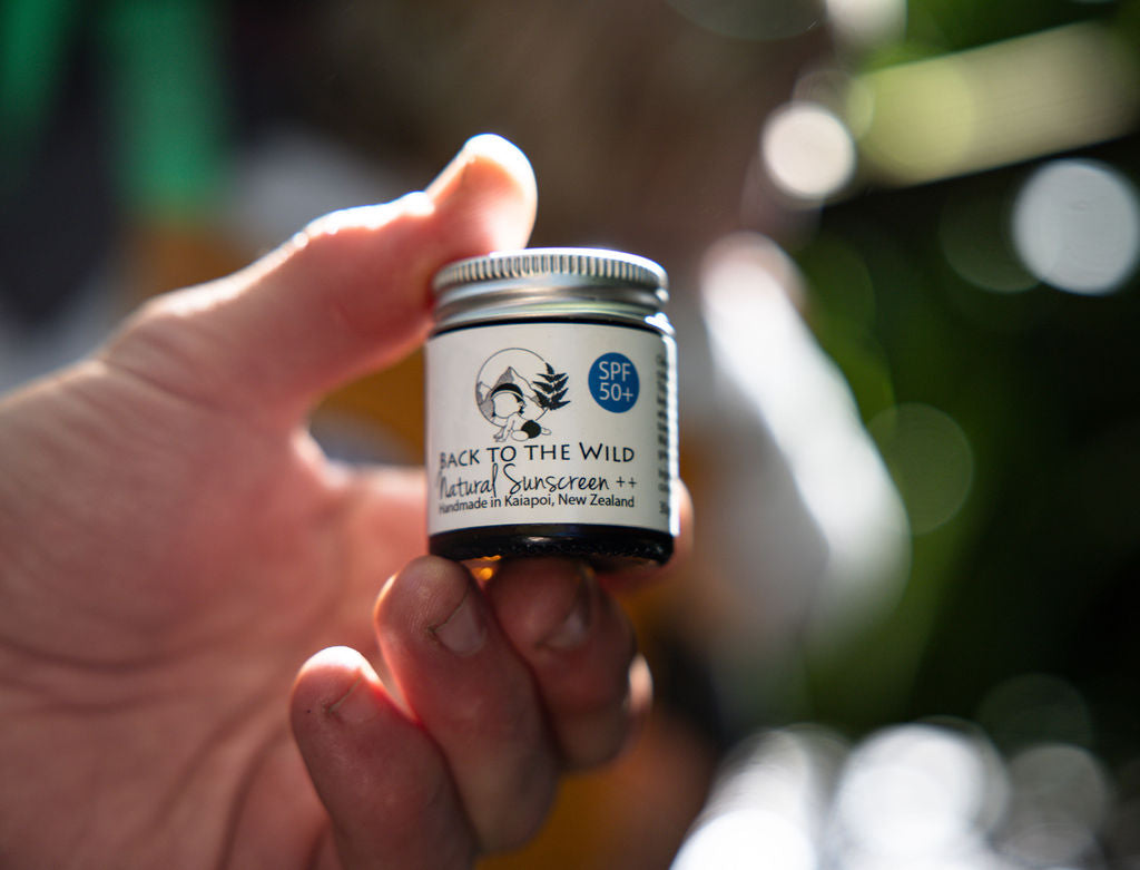 Hand holding a small jar of 'Back to the Wild' natural sunscreen with a blurred outdoor background.