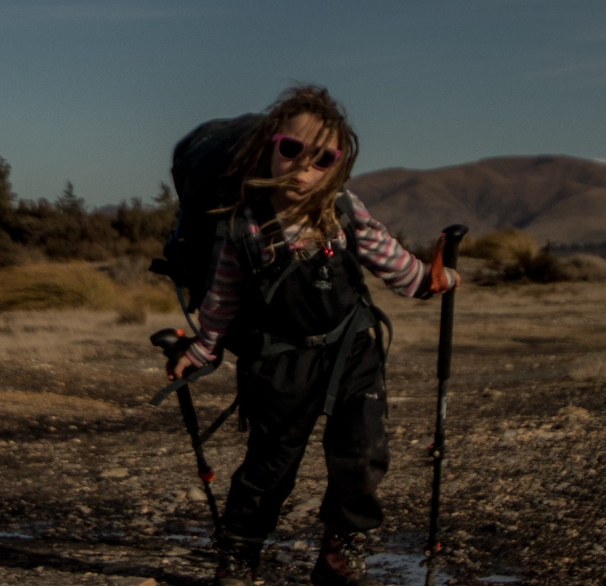 Child wearing sunglasses hiking in a desert landscape with mountains in the background
