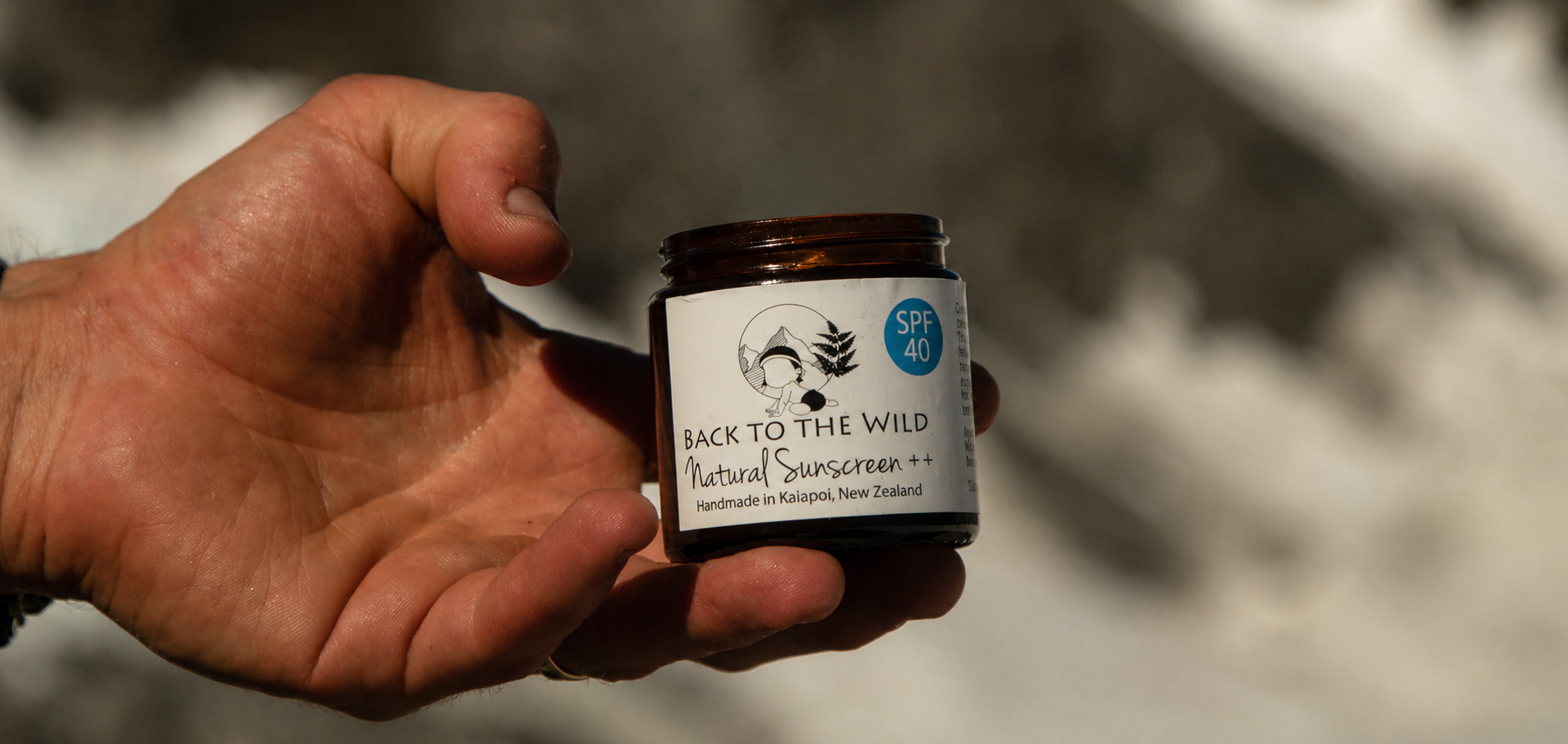 Hand holding a jar of 'Back to the Wild' natural sunscreen with a blurred background