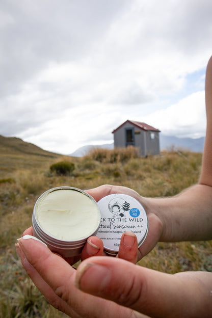 Person holding containers of 'Back to the Wild' natural sunscreen in a scenic outdoor setting.