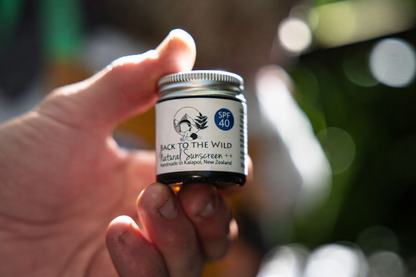 Hand holding a small jar of 'Back to the Wild' natural sunscreen with a blurred outdoor background.