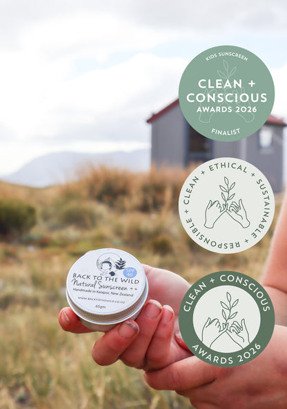 Hand holding a small container of natural sunscreen with 'Back to the Wild' branding, set against a scenic background.